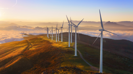 Wind turbines on a ridge at sunrise, producing green energy; golden light, clouds below.