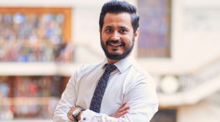 Man in white shirt and tie with arms crossed, smiling in a modern building.