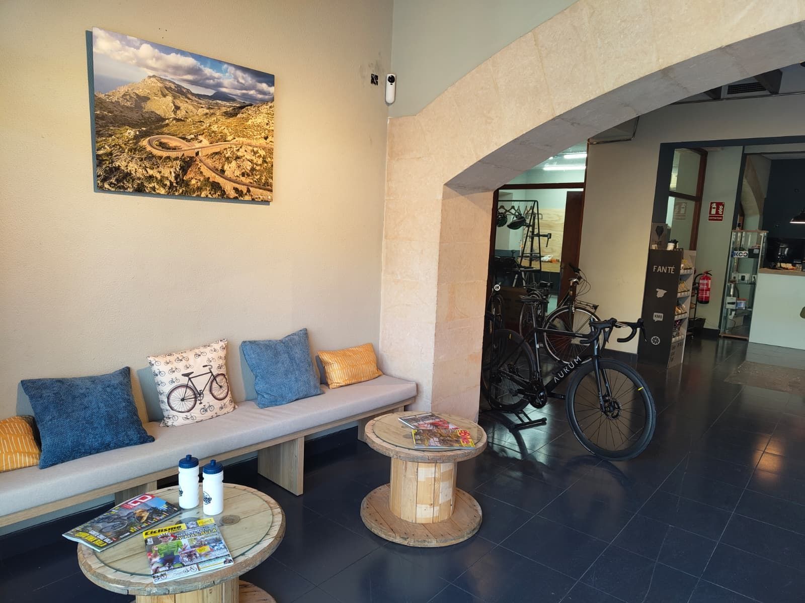 Zona de descans amb bancs, taules de fusta i una foto d'un paisatge de muntanya. Hi ha una bicicleta a prop.