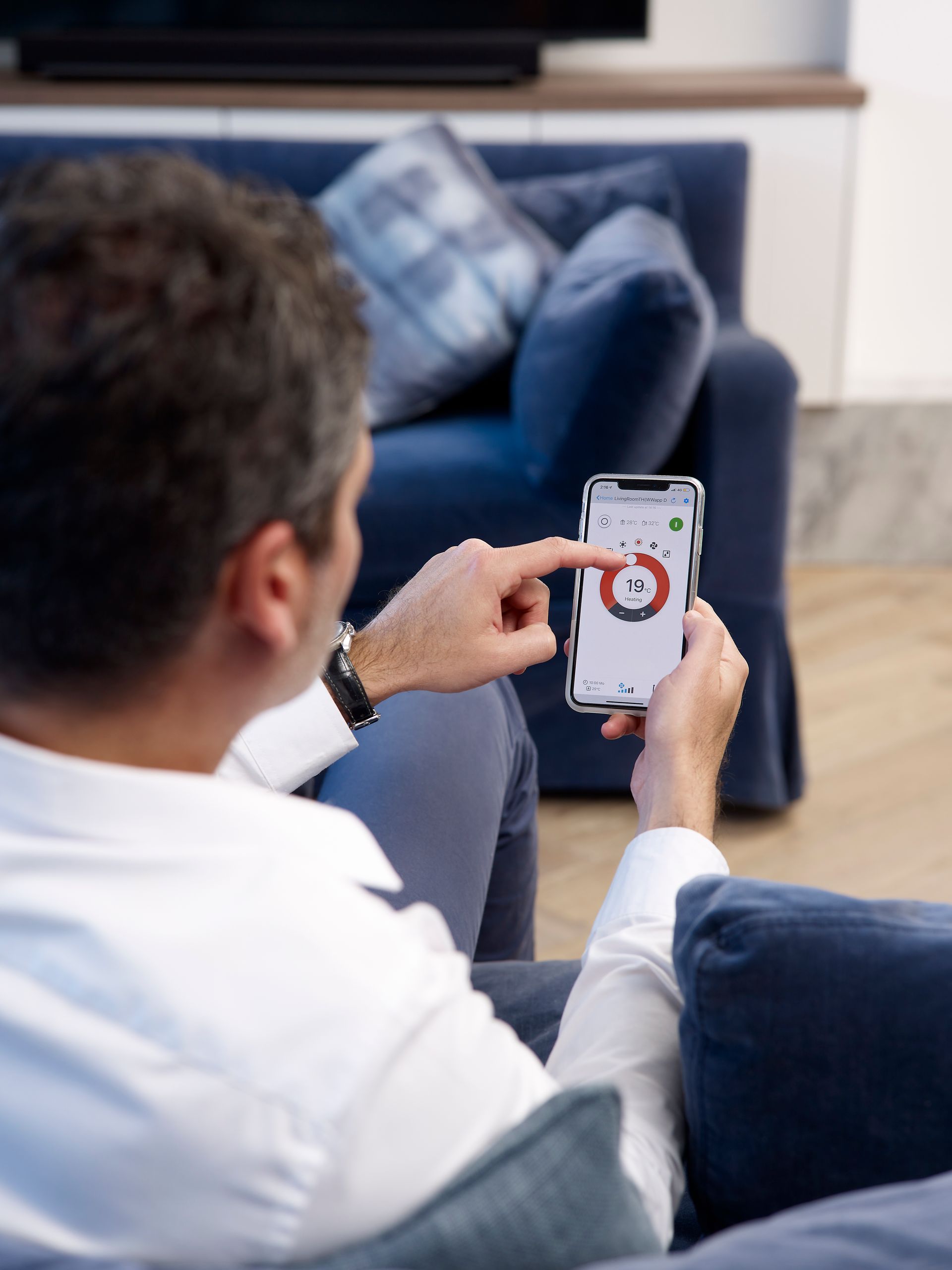 A Male Adjusts an Aircon Using a Mobile Device While Seating on a Blue Couch | Batemans Bay, NSW
