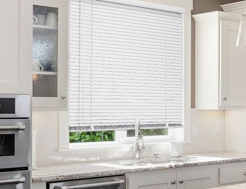 White blinds in kitchen window, over a sink and white cabinets.