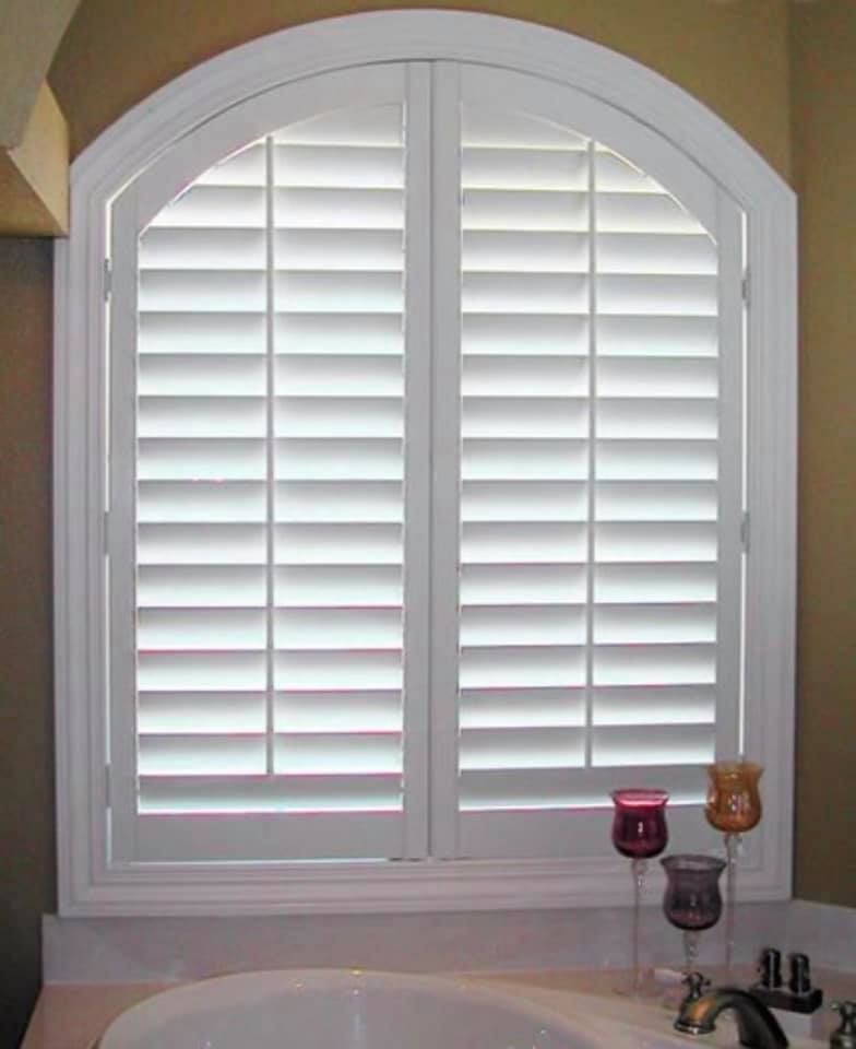 White arched window shutters in a bathroom, over a white sink and countertop.