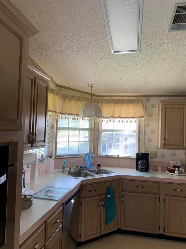 Kitchen with light-colored cabinets, pink countertops, and a window with curtains above the sink.