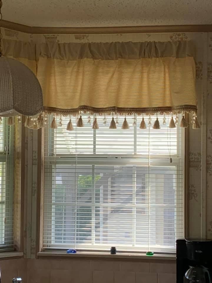 Yellow window valance with tassels above a window with blinds.