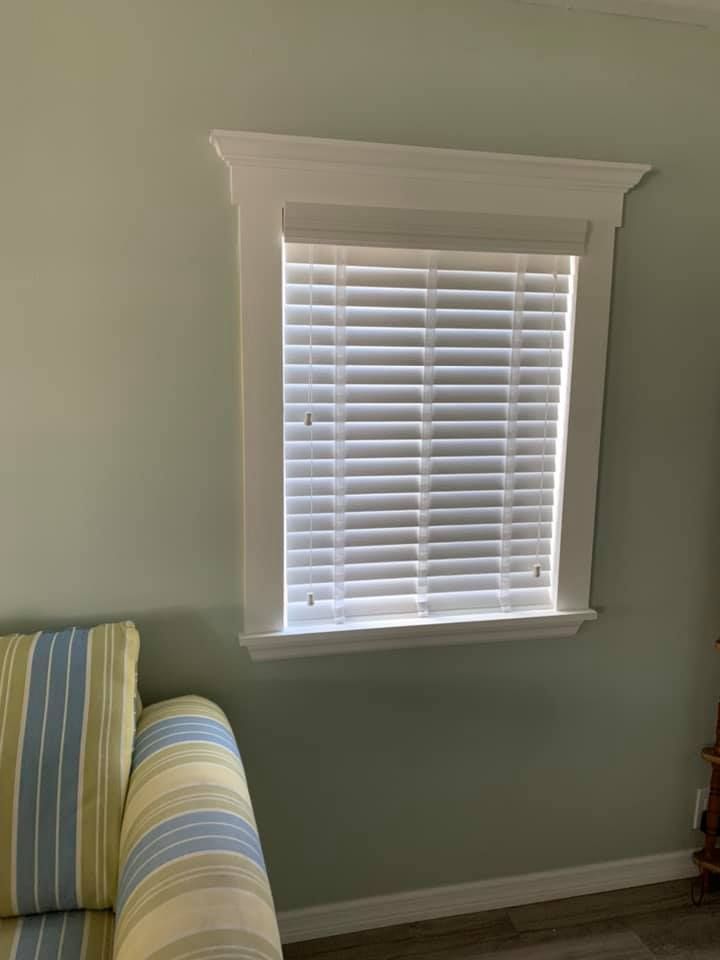 Window with white blinds and trim on a light green wall, next to a striped sofa.