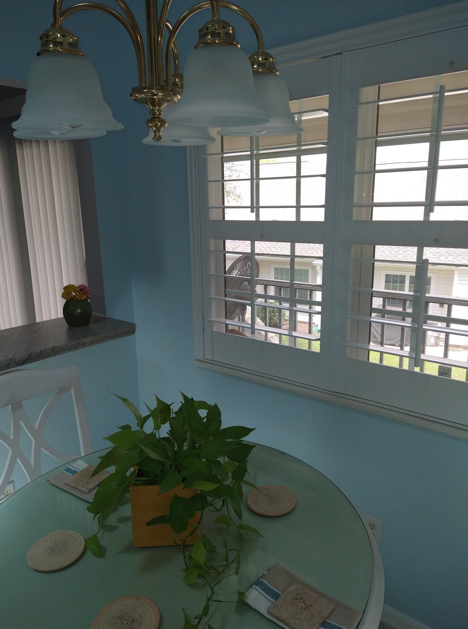 A round table with a plant, coasters, and window with a trellis. Blue walls, chandelier above.