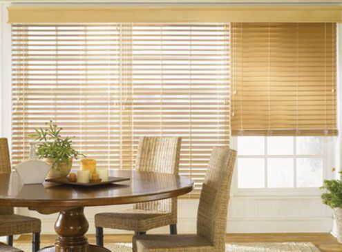 Dining room with wooden blinds, round table, woven chairs, and plants.