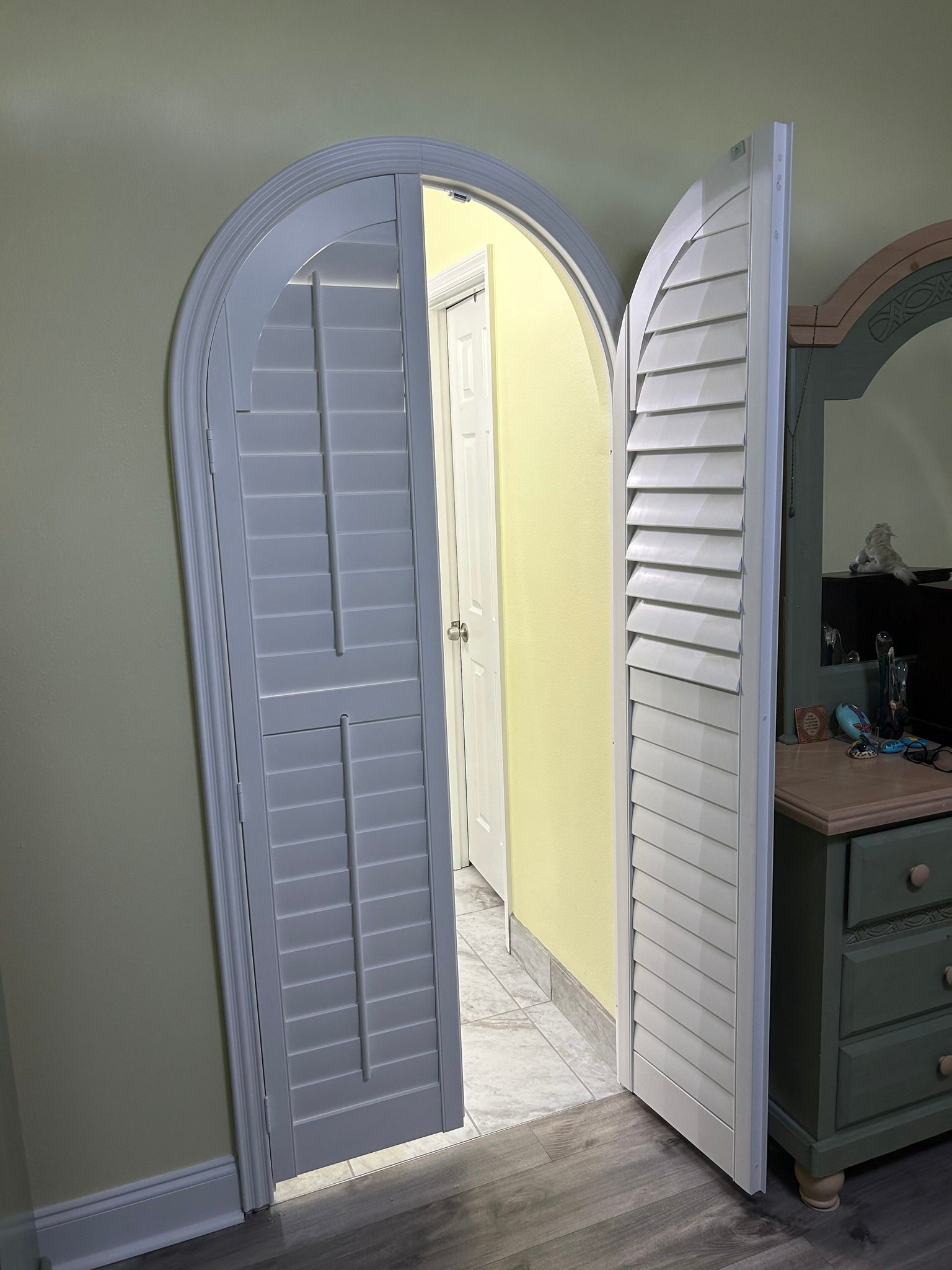 Arched doorway with white shutters open to a bathroom, next to a green dresser.