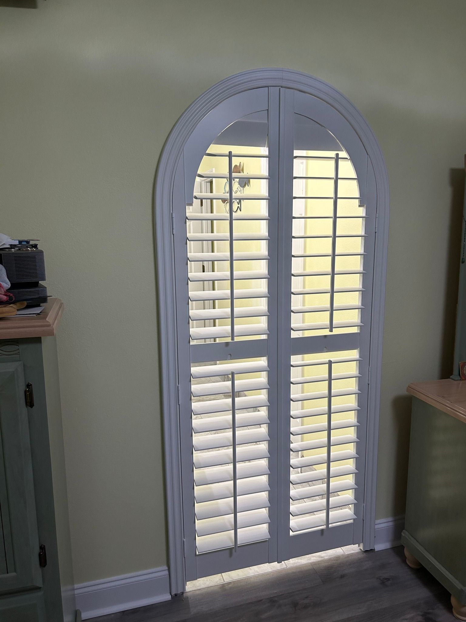 Arched white shutters on a doorway, yellow wall, green and beige furniture.