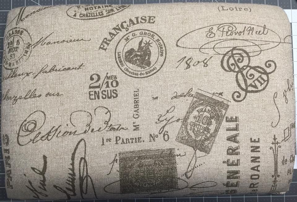 Close-up of a rectangular fabric piece with beige background and French script and stamps in brown.