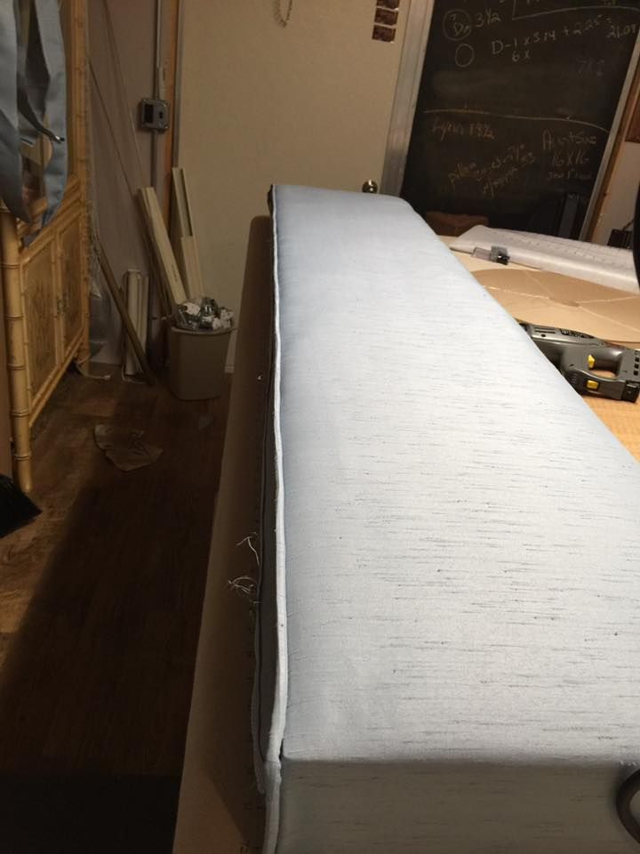 Light gray upholstered bench on a wooden surface, with tools and a chalkboard visible in the background.