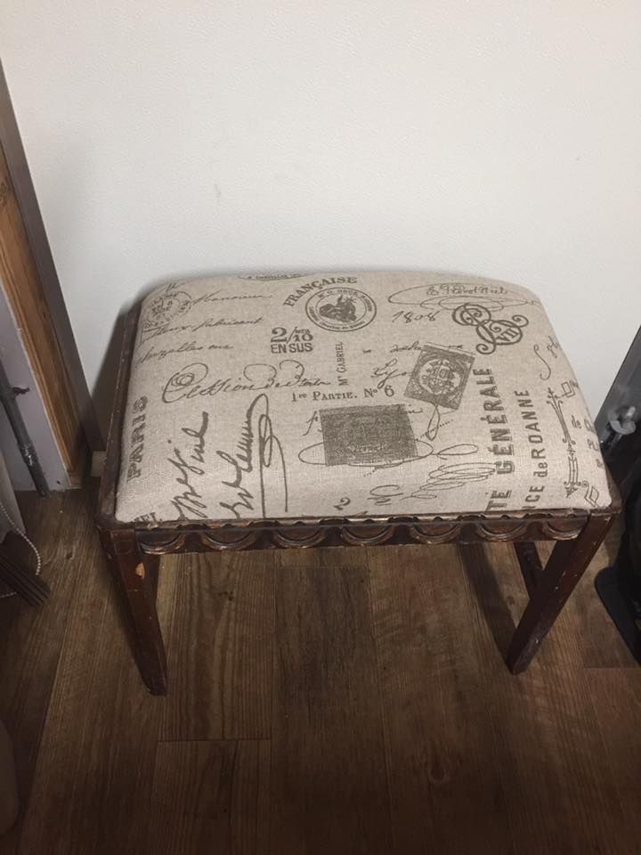 Vanity stool with cream-colored fabric seat featuring script and stamps, on a brown wooden frame.