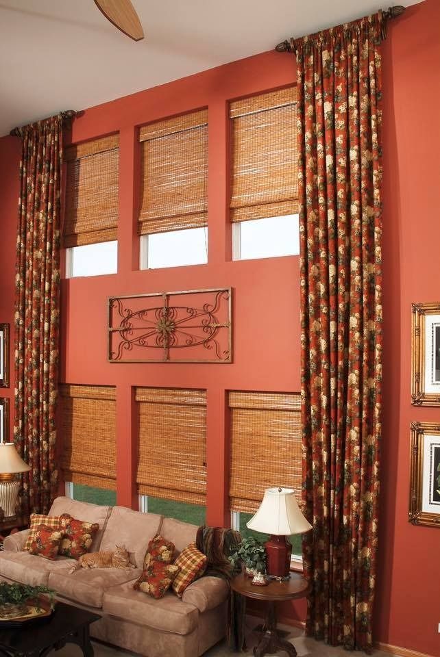 Living room with orange wall, windows with woven blinds, floral drapes, and a sofa with pillows.