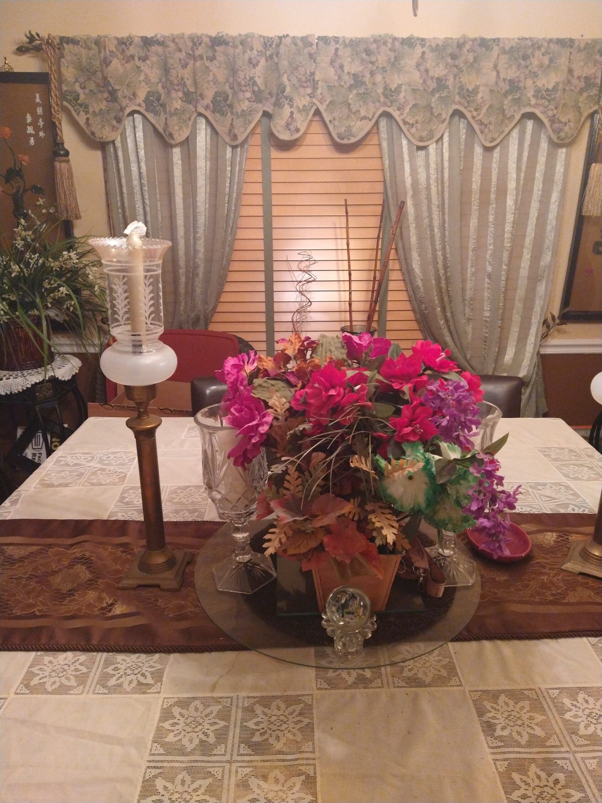Dining table with floral centerpiece, candleholder, and window with floral curtains.