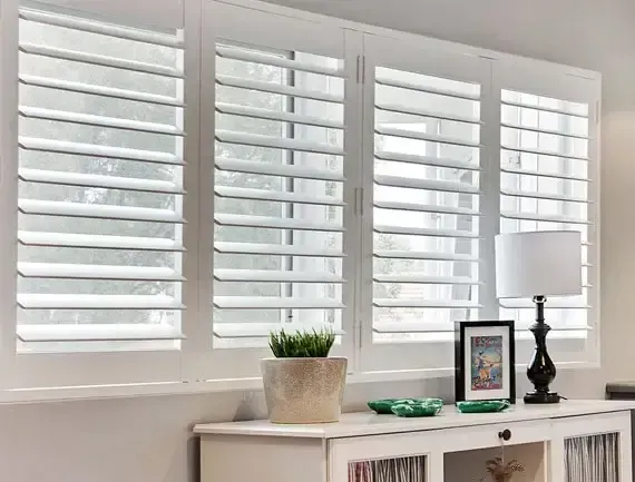 White shutters over windows with a console table featuring a lamp and decor.