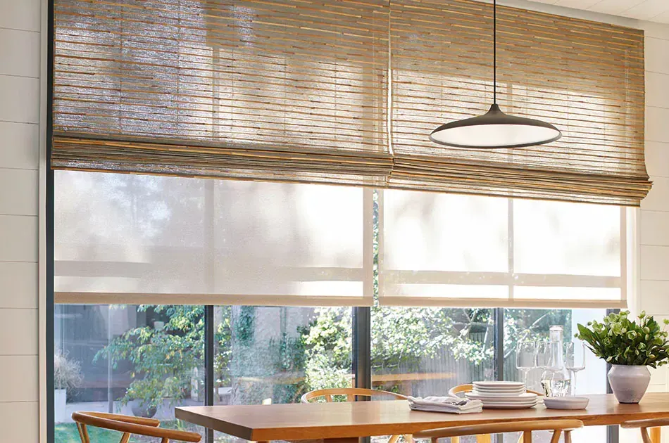 Dining room window with layered shades: woven top and light-filtering bottom, overlooking greenery.