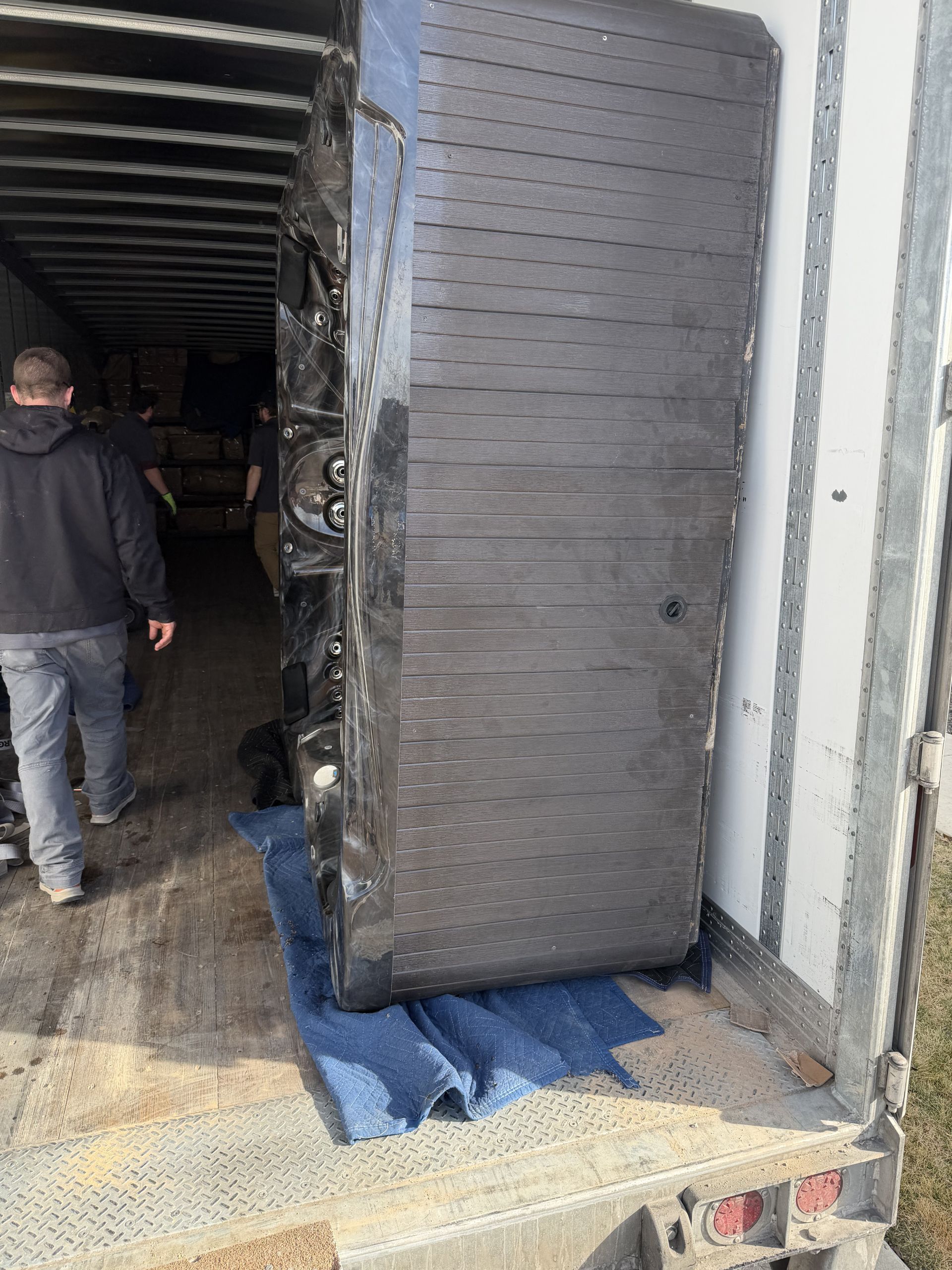 A large, wrapped black item, possibly furniture, being unloaded from a truck by two people.