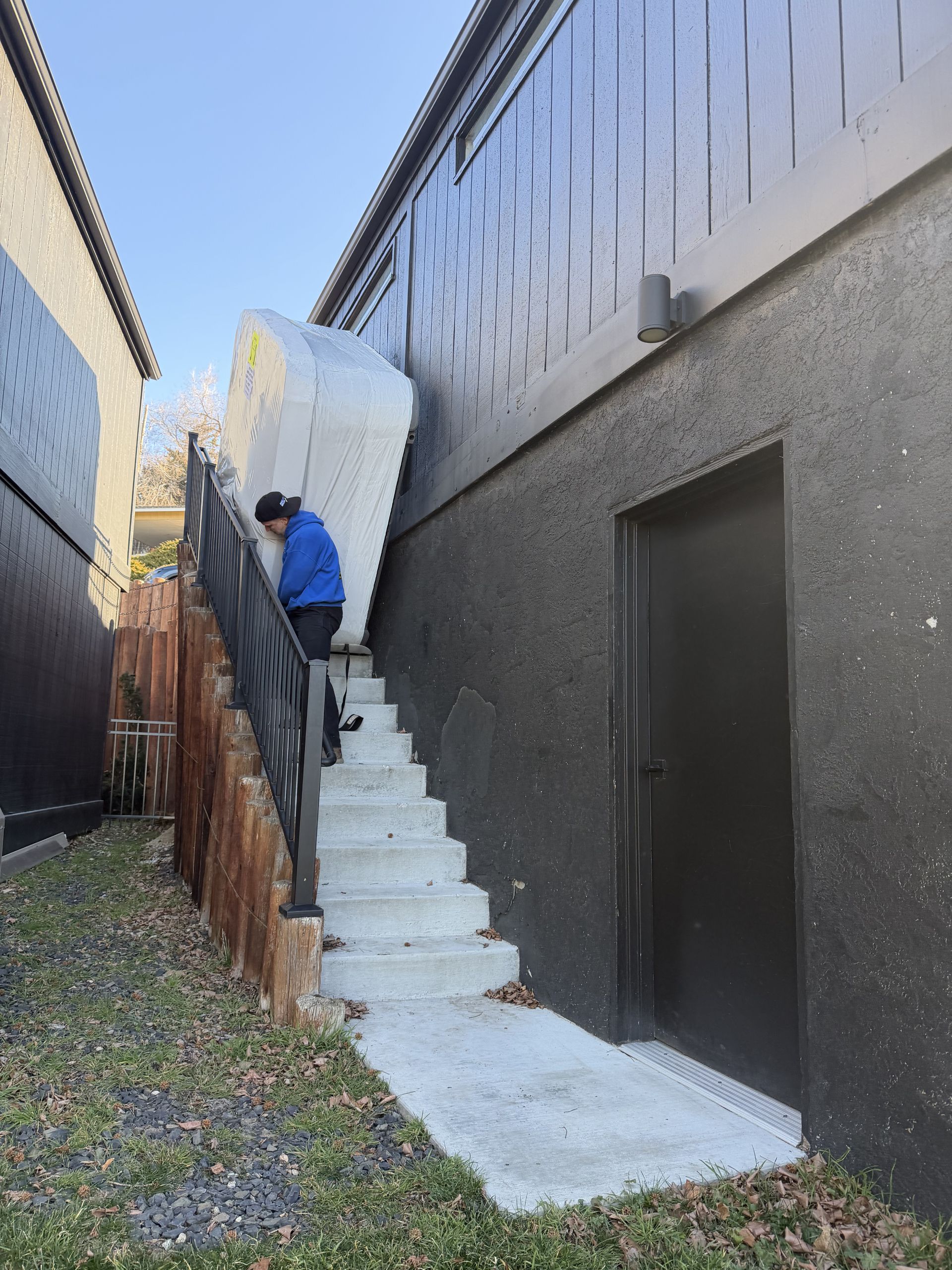Person carrying large, white object up outdoor stairs next to a black building.