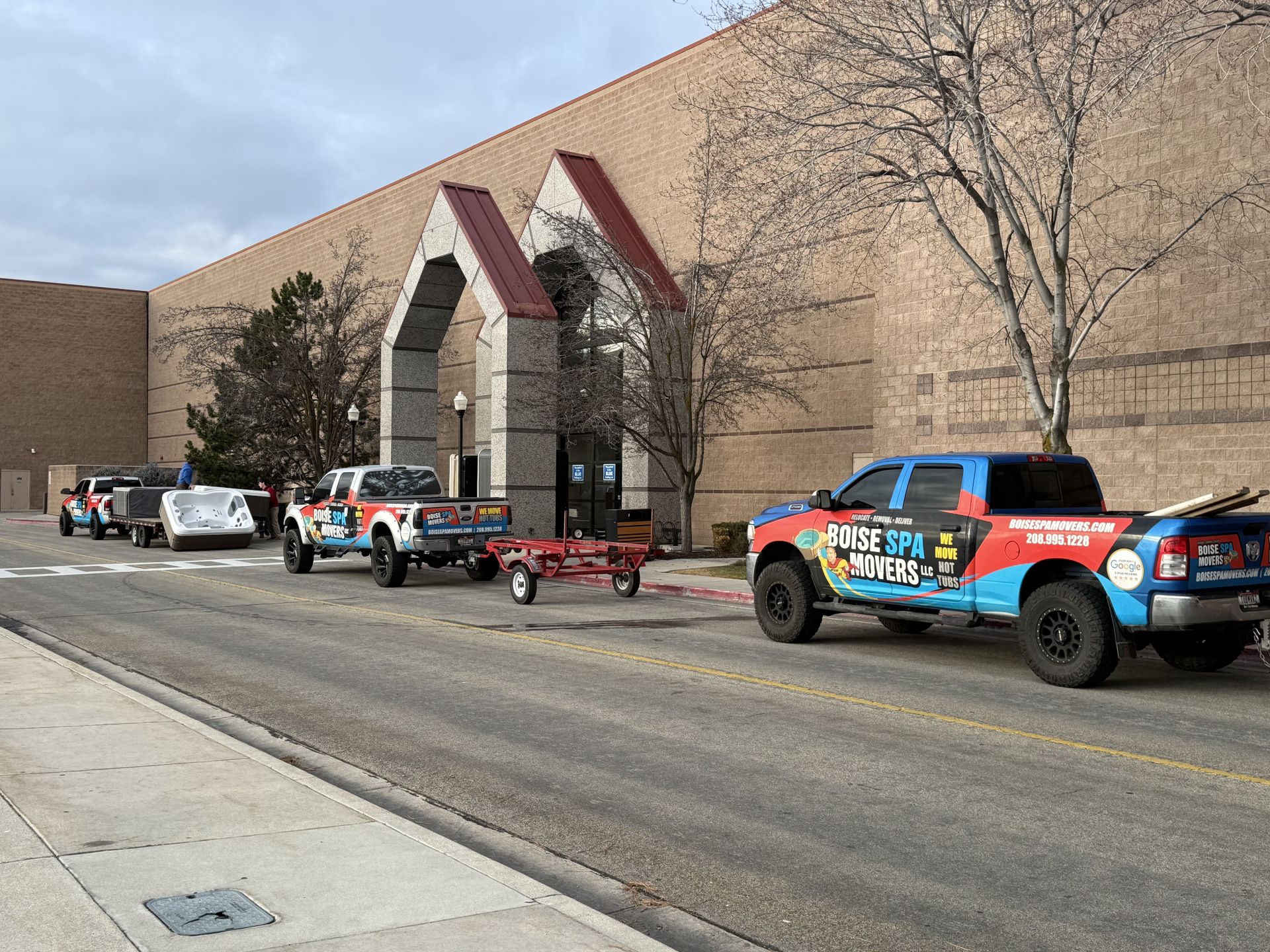 Several pickup trucks and trailers parked outside a brick building with arched entrance.