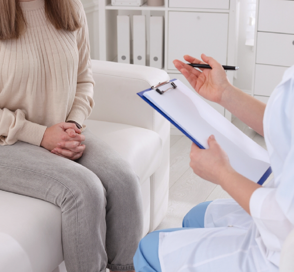 A woman is sitting in a chair talking to a doctor who is holding a clipboard