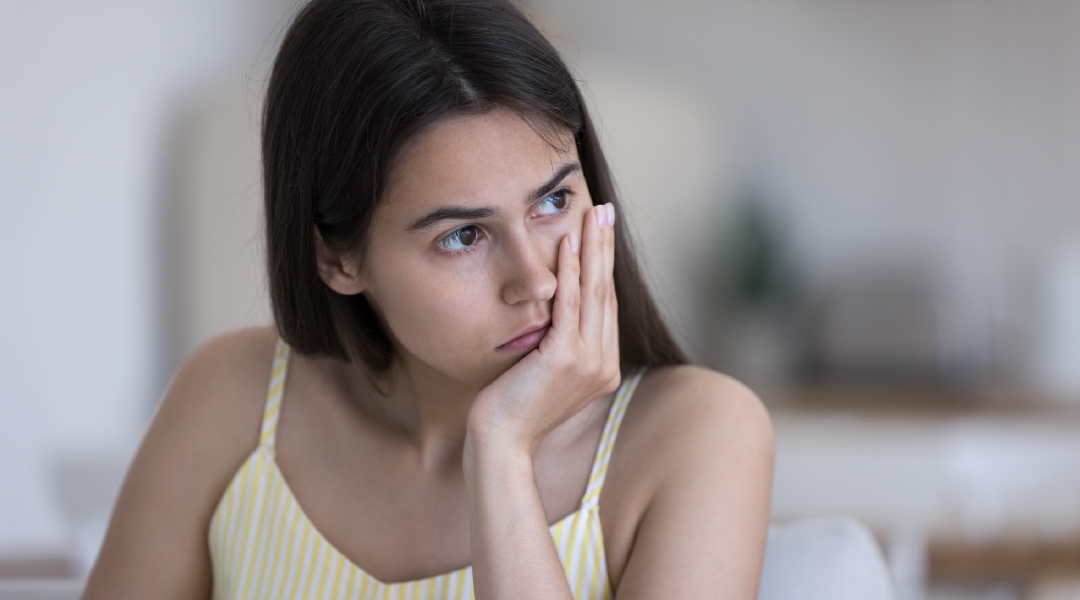 A woman is sitting on a couch with her hand on her face.