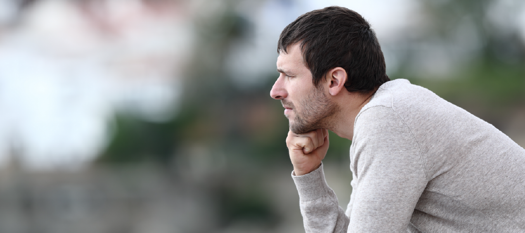 A man is sitting down with his hand on his chin.