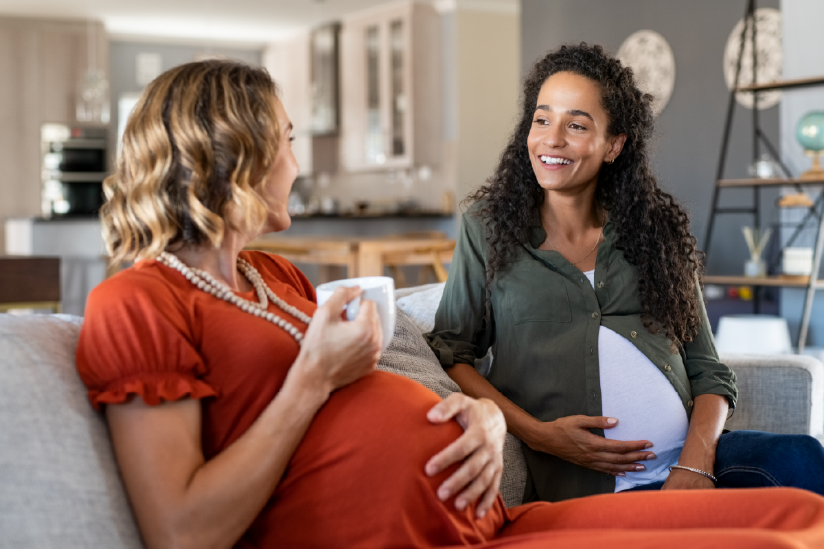 A pregnant woman is sitting on a couch talking to another woman.