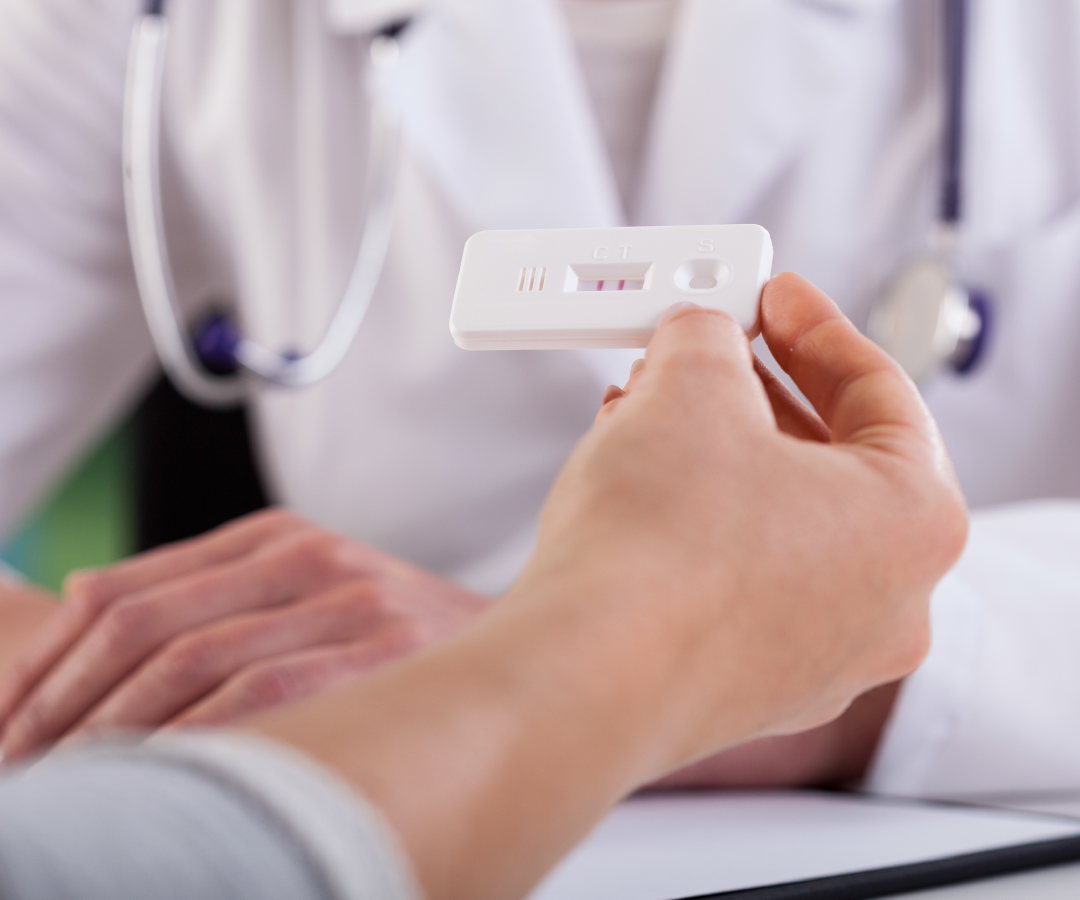 A woman is holding a pregnancy test in front of a doctor.