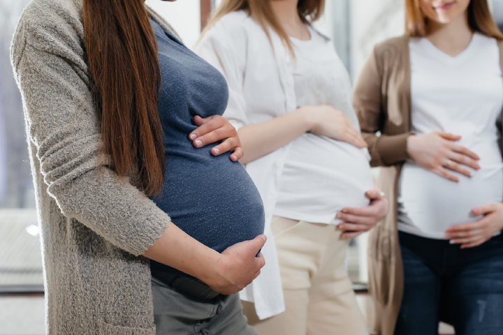 Three pregnant women are standing next to each other holding their bellies.