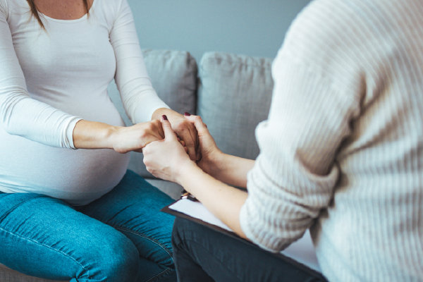 A pregnant woman is holding hands with a man while sitting on a couch.