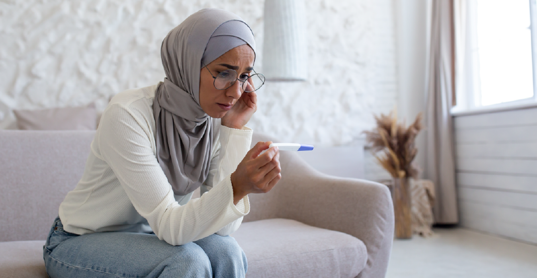 A woman in a hijab is sitting on a couch holding a pregnancy test.