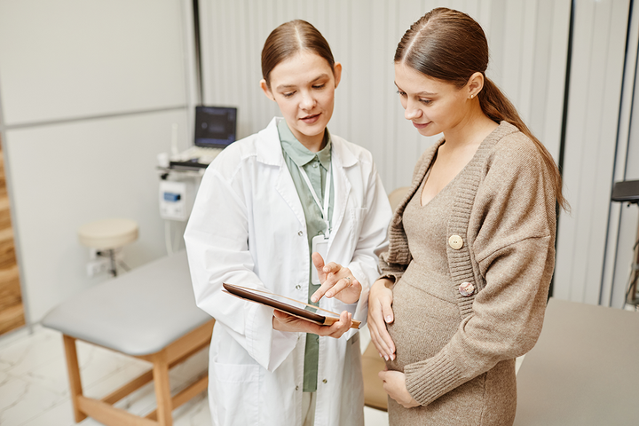 A pregnant woman is talking to a doctor who is holding a tablet.