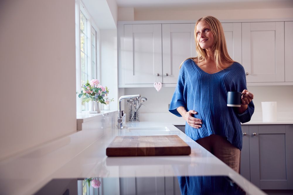 A smiling older pregnant woman holding a mug.