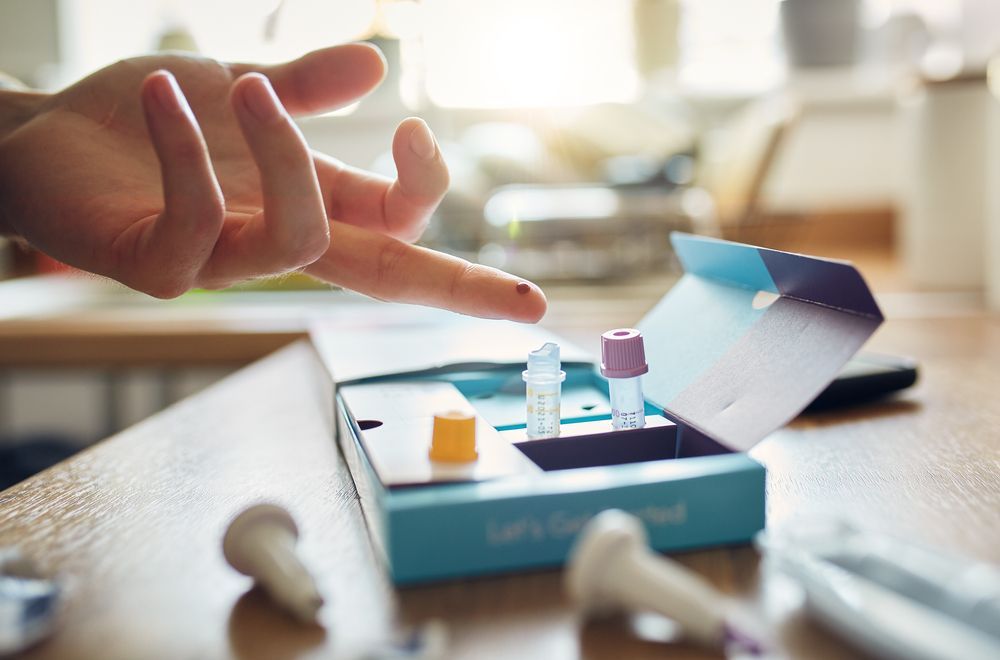 Person collecting blood sample from finger with home test kit.