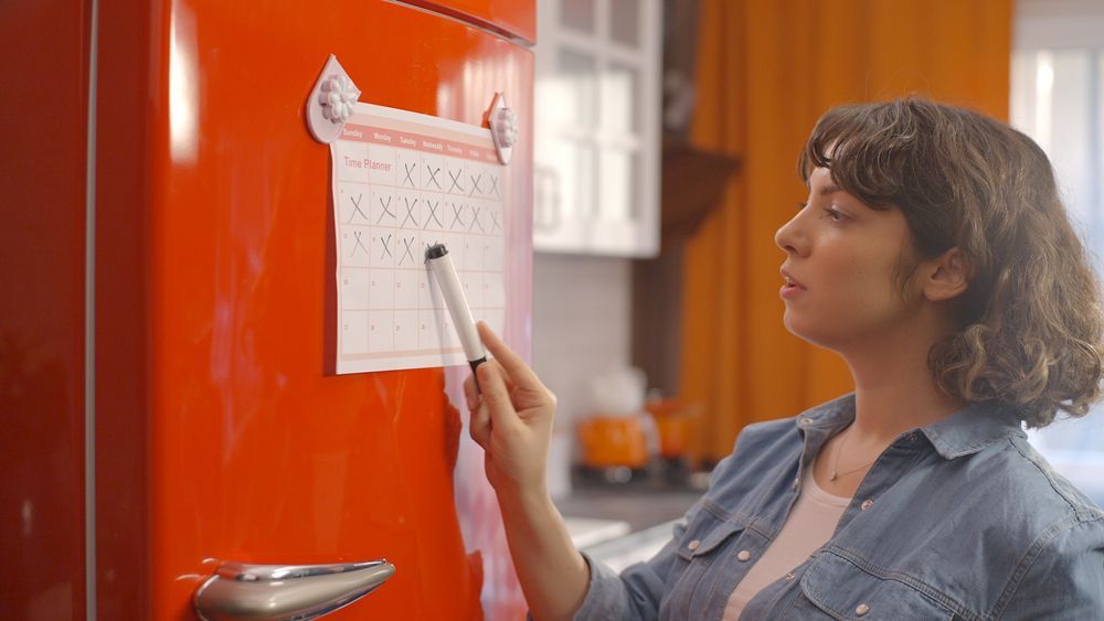 Woman marking a calendar on a red refrigerator with a marker.