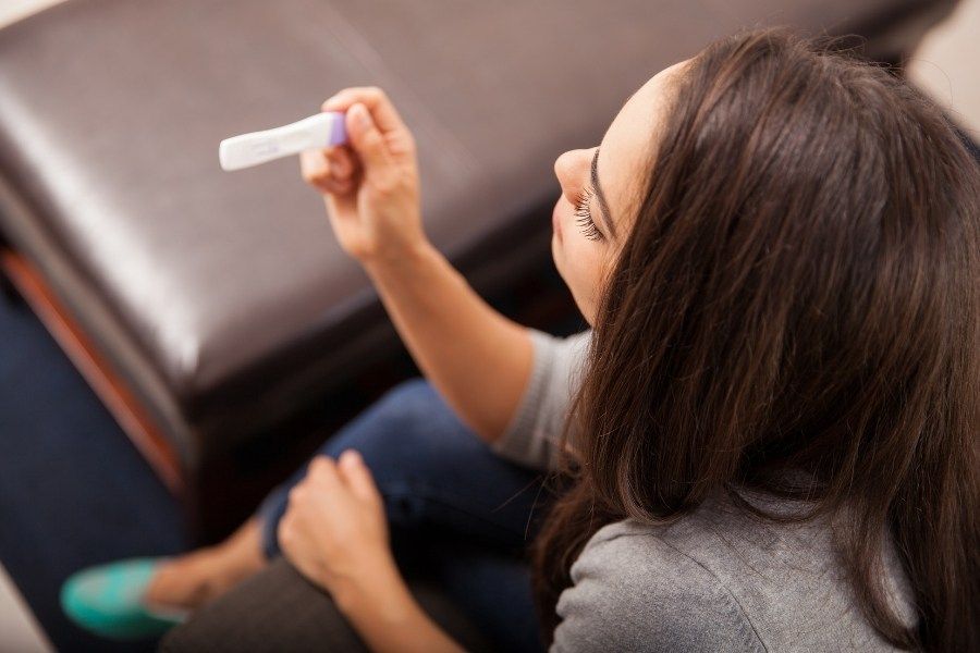 A woman is sitting on a couch holding a pregnancy test.