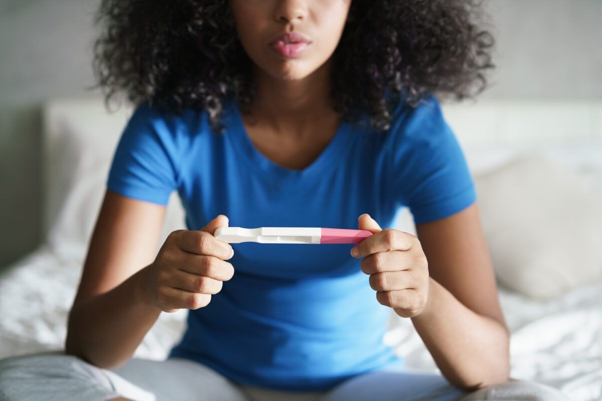 A woman is sitting on a bed holding a pregnancy test.