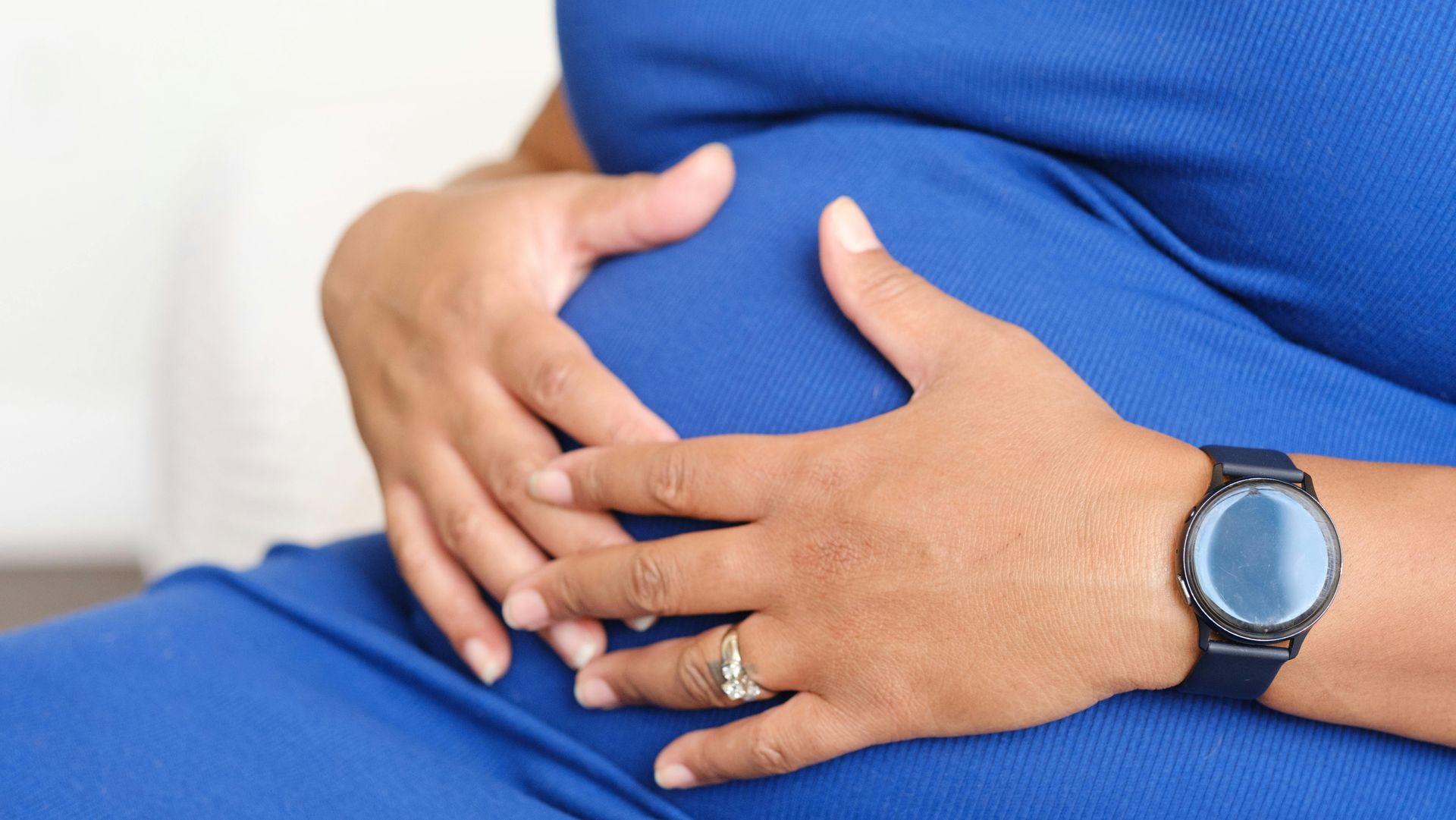 Hands resting on a pregnant belly, with one hand wearing a watch and a ring.
