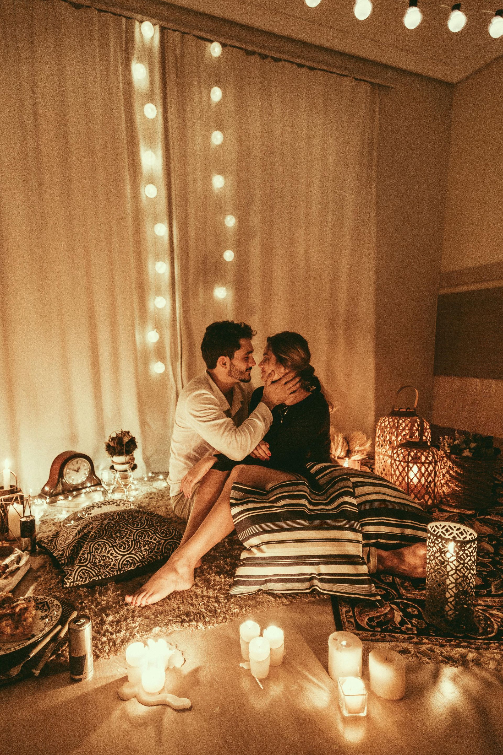 A man and woman holding each other on a bed, surrounded by candles and mood lighting.