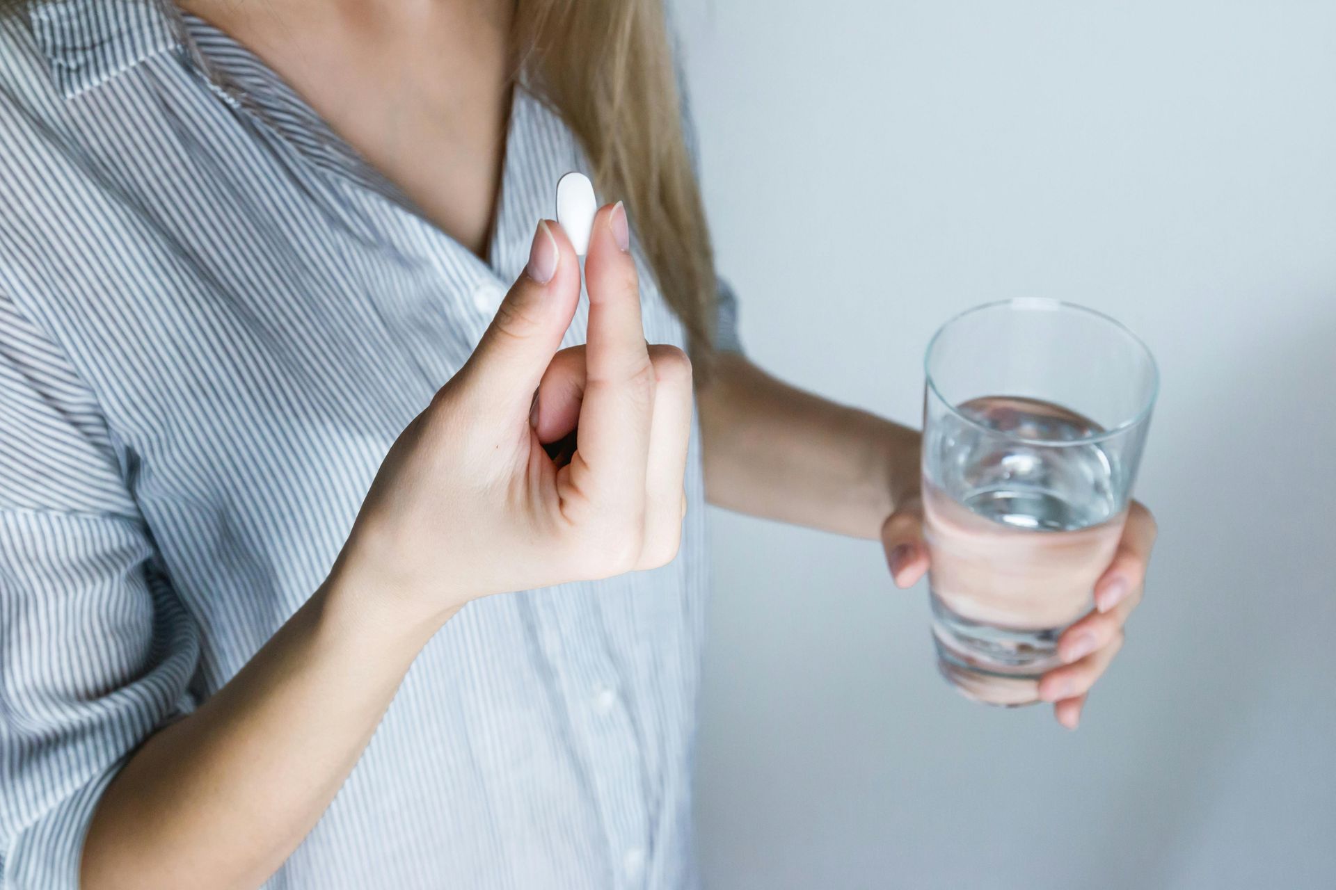 Woman holding pill between fingers, and glass of water, indoors.