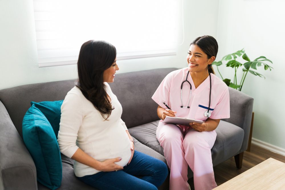 A pregnant woman is sitting on a couch talking to an OB-GYN.