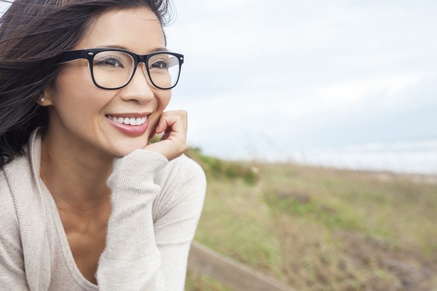 A woman wearing glasses is smiling in a field.