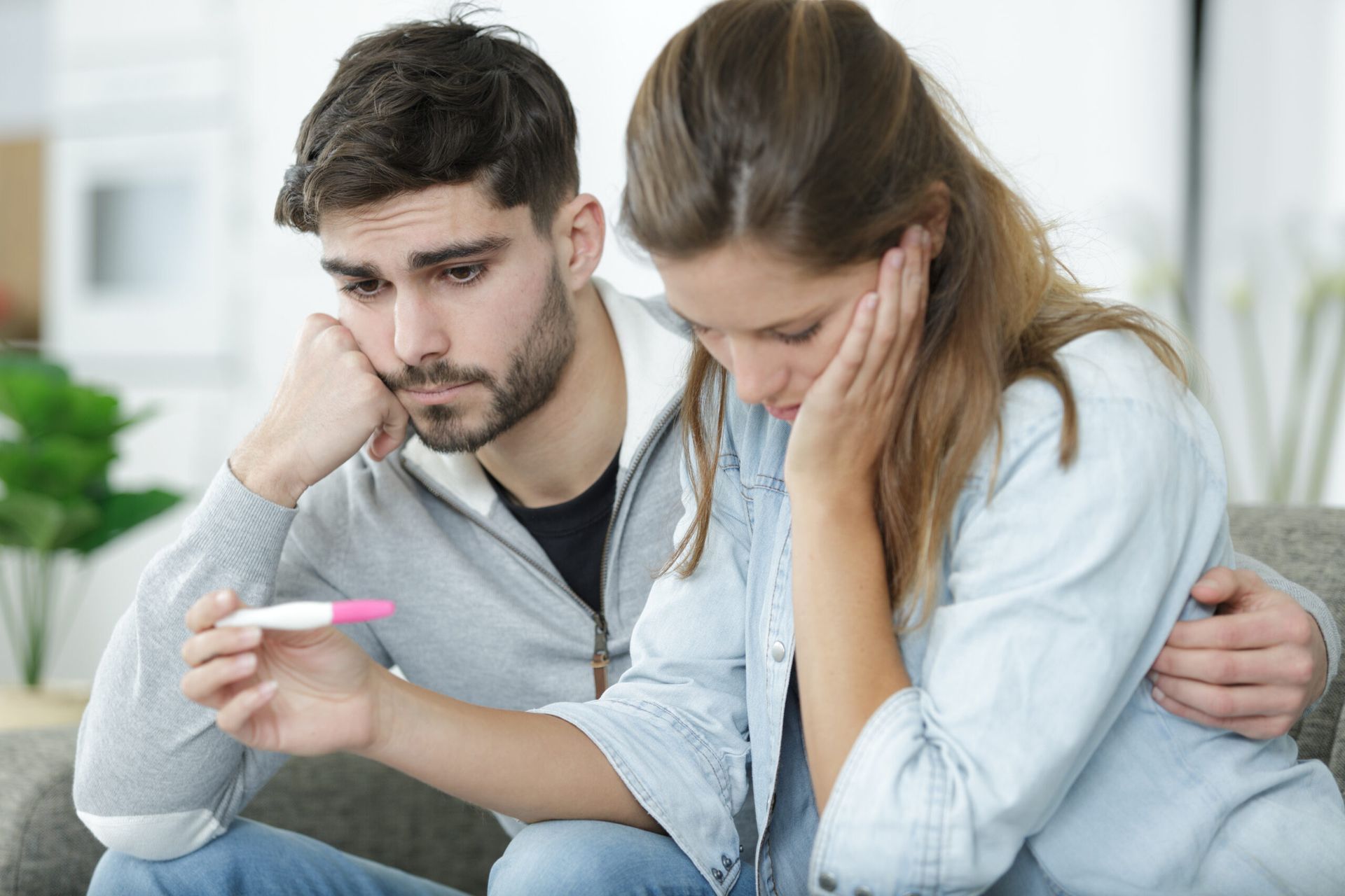 A man and a woman are sitting on a couch looking at a pregnancy test.