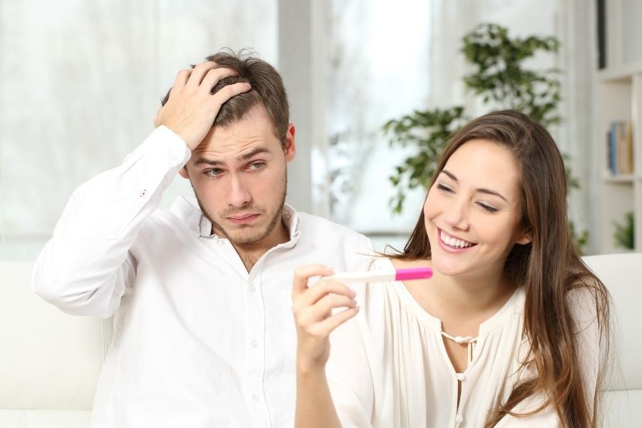 A man and a woman are sitting on a couch looking at a pregnancy test.