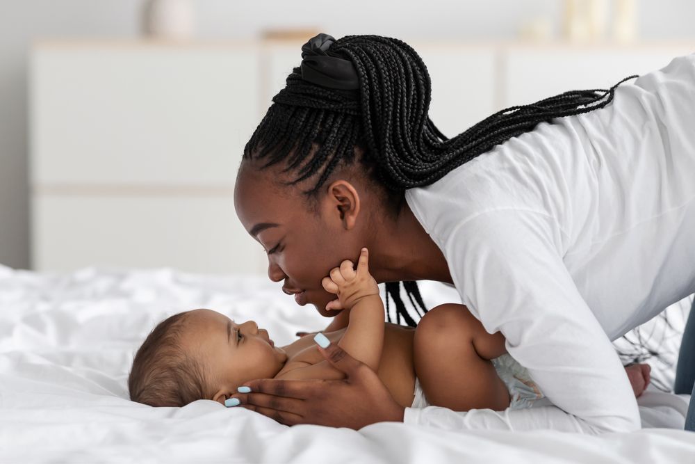 A woman is playing with her baby on a bed.