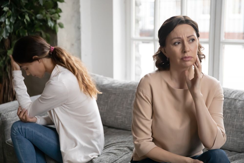 A mother and daughter are sitting on a couch with their backs to each other.