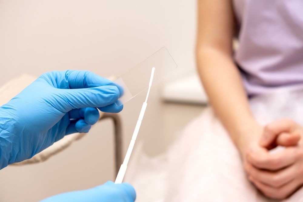 A doctor is holding a swab in front of a woman sitting on a toilet.