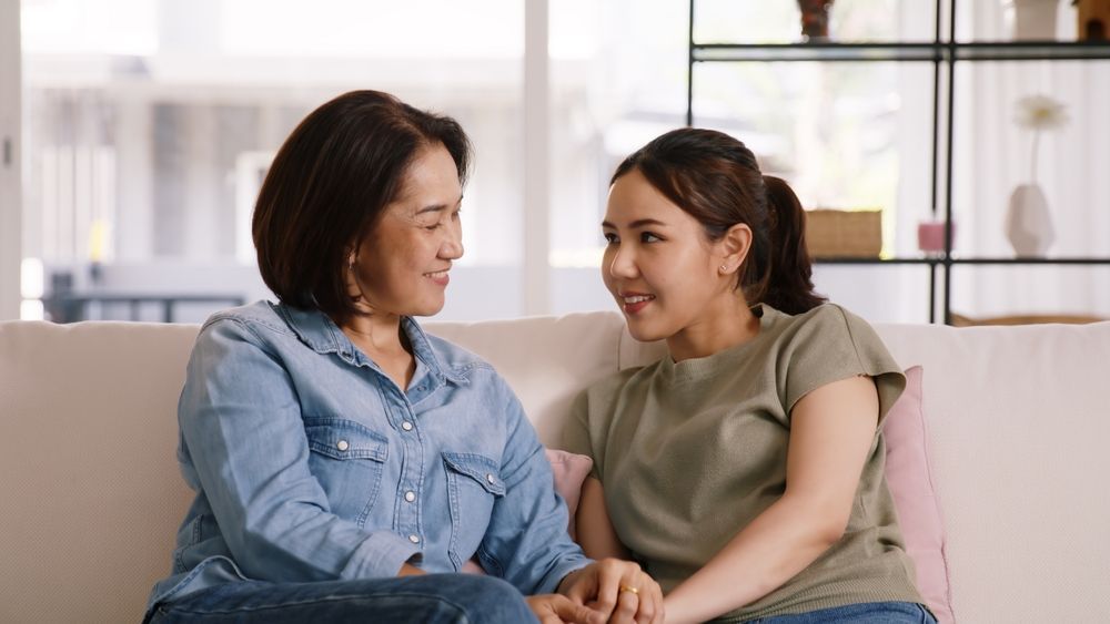 Two women are sitting on a couch holding hands and talking to each other.