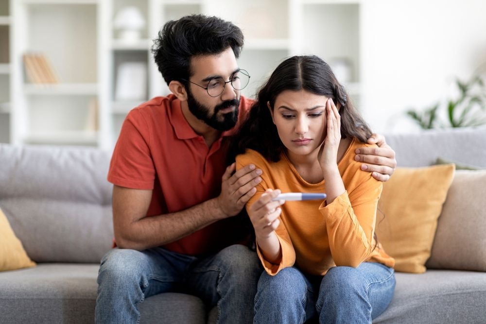 A man is comforting a woman who is holding a pregnancy test.