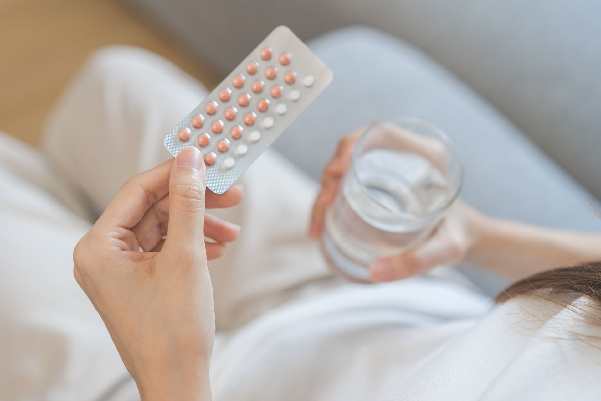 A woman is holding a blister pack of pills and a glass of water.